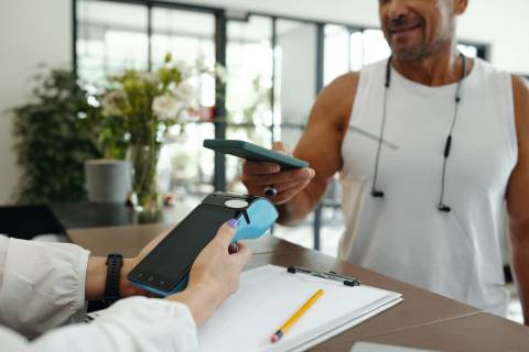 Smiling man making a swift contactless payment at a UK health and beauty POS terminal in a modern fitness center reception.