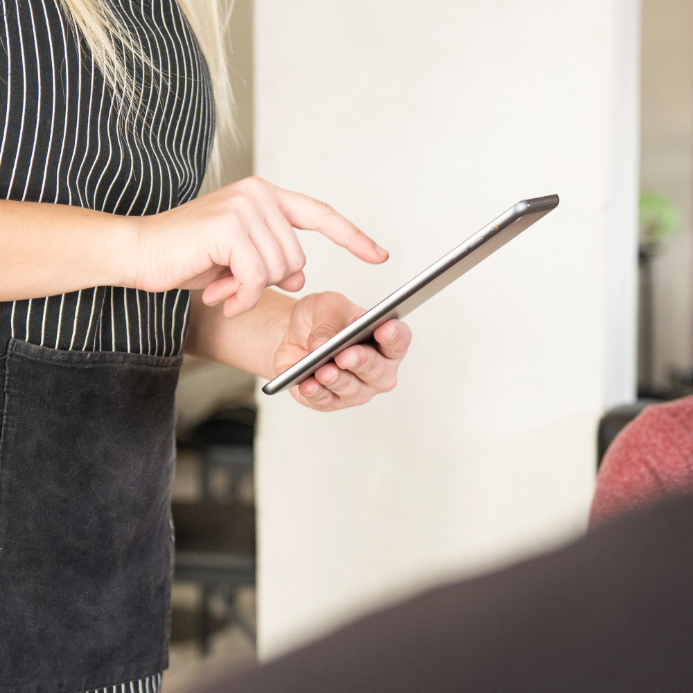A close-up shot of a person wearing a striped apron, using their finger to interact with a digital tablet